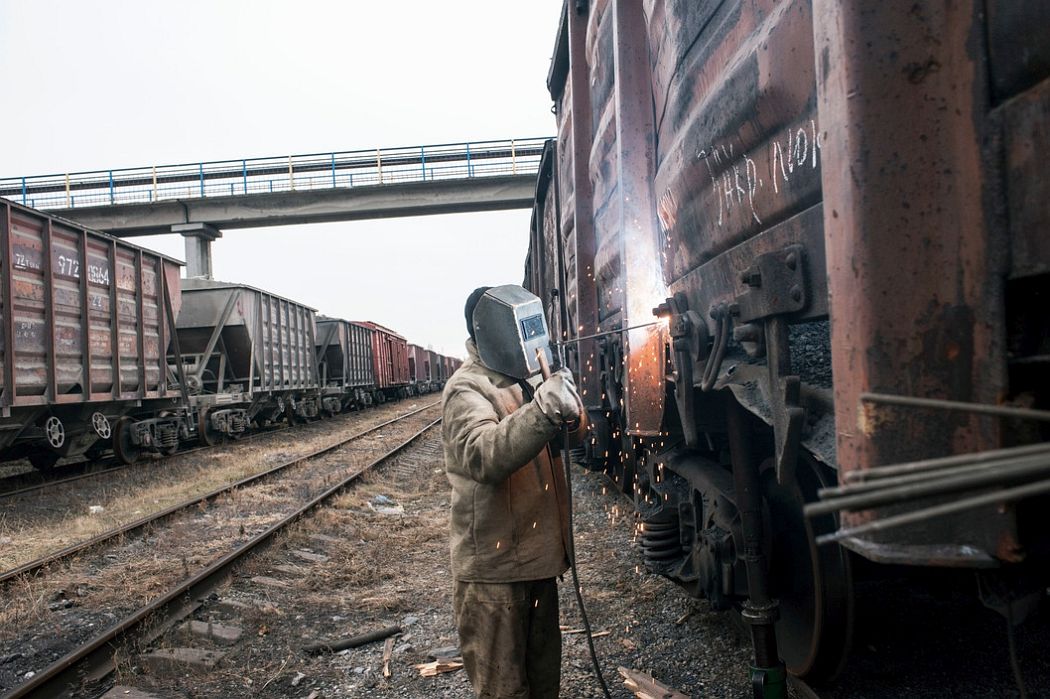 UKRAINE. Ilovaisk, East Ukraine. November 25, 2014. A welder repairs freight trains damaged by separatist shelling of a train yard when it was occupied by the Ukrainian army, in what is now a separatist strong hold.