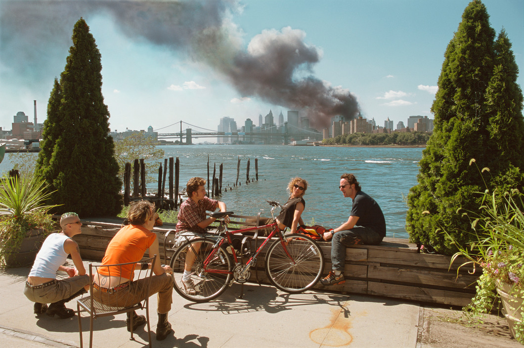 USA. Brooklyn, New York. September 11, 2001. Young people relax during their lunch break along the East River while a huge plume of smoke rises from Lower Manhattan after the attack on the World Trade Center.