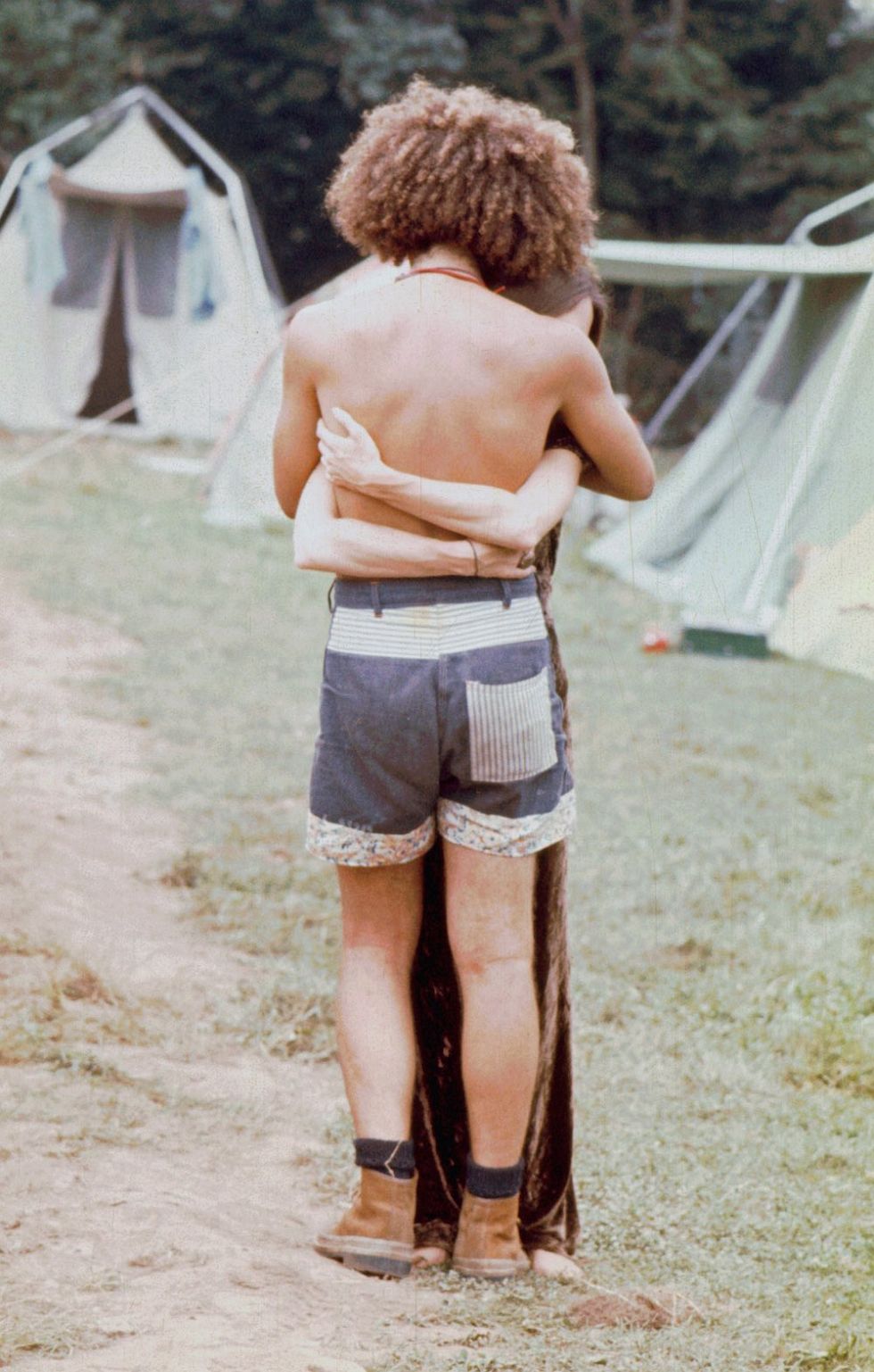 One of the dancers hugs someone on the dirt road as they stand near the tents.